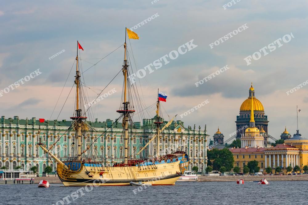 На фотографии изображен исторический парусный фрегат на Неве, рядом с которым виднеется Зимний дворец (Эрмитаж). Золотой купол Исаакиевского собора и шпиль Адмиралтейства дополняют композицию, отражая величие архитектуры Санкт-Петербурга. Летний день подчеркивает насыщенные цвета и детали, создавая яркую и запоминающуюся картину. Этот вид на центр города воплощает в себе красоту и историческое наследие Санкт-Петербурга.